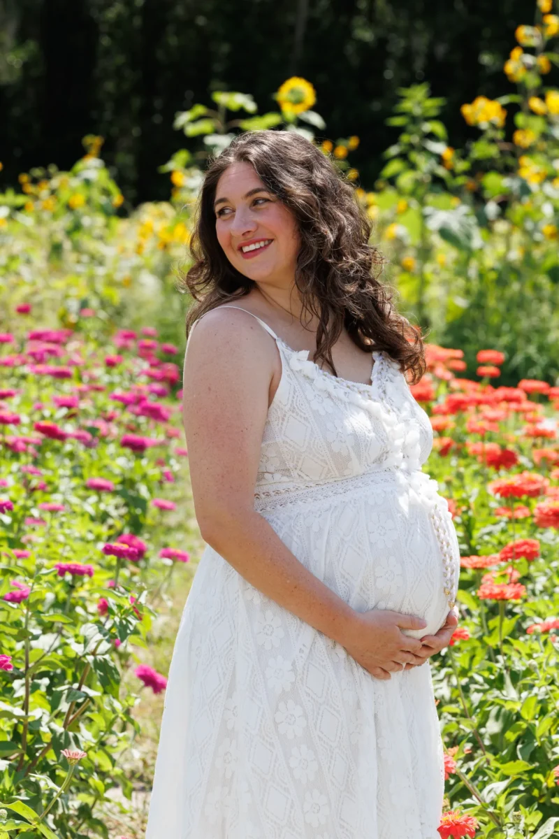 A pregnant woman in a white dress stands among vibrant flowers, cradling her belly in a sunny, blooming garden. A pregnant woman in a white dress stands among vibrant flowers, cradling her belly in a sunny, blooming garden.