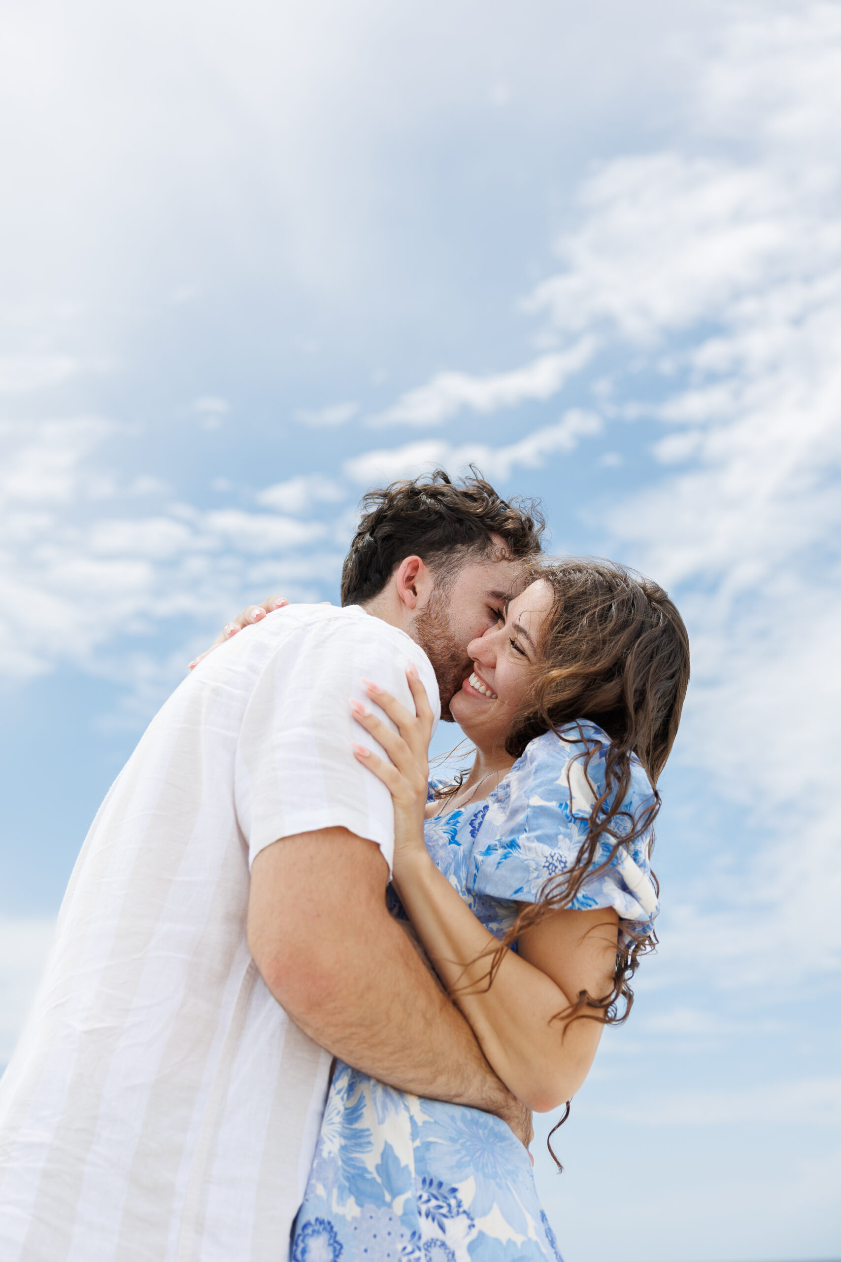 7N4A9100 A close-up of a bride and groom holding hands, showcasing their wedding bands and elegant attire against a softly lit background.