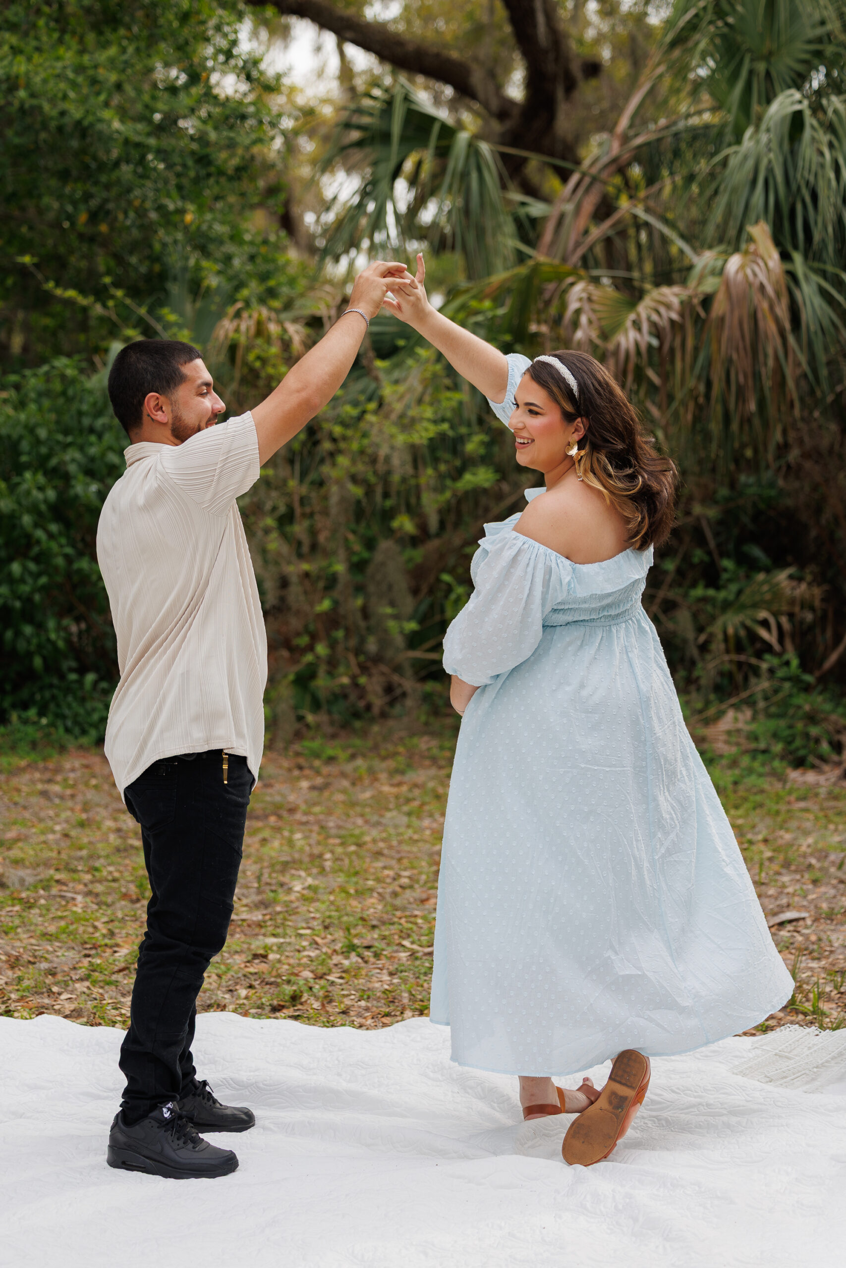 LO1A2004 A pregnant woman in a white dress stands among vibrant flowers, cradling her belly in a sunny, blooming garden.