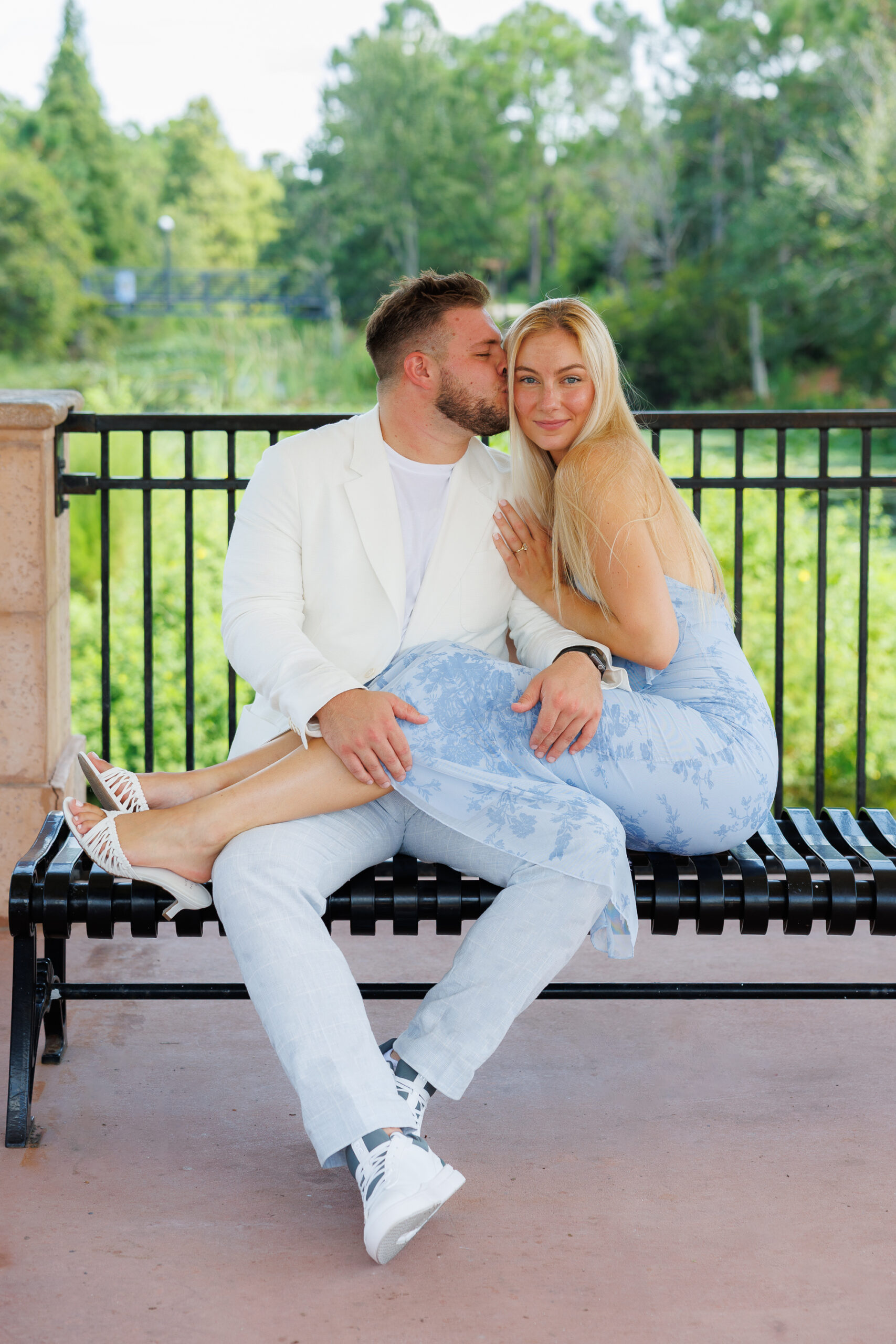Couple sitting on a blanket, holding a letter board that announces "Baby Mateo 2025" with decorative hearts